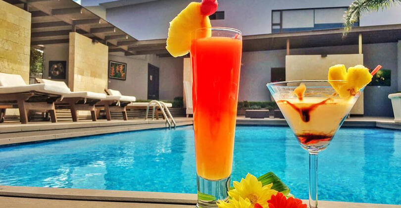Picture of a tropical drink next to the pool of the Costa Rica Medical Center Inn, San Jose, Costa Rica.  The drink is tropical red and yellow with an orange slice at the top. The background is a blue pool.