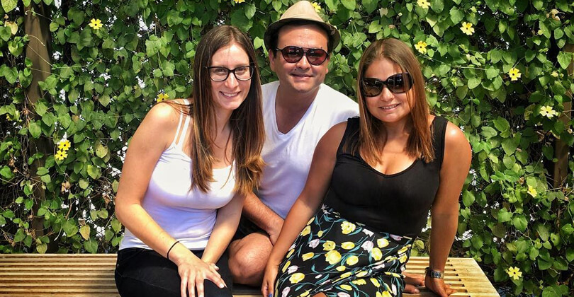 Picture of three guests enjoying their stay at the Costa Rica Medical Center Inn in San Jose, Costa Rica.  The guests are grouped together on an outdoor bench with trees behind them and are smiling at the camera.