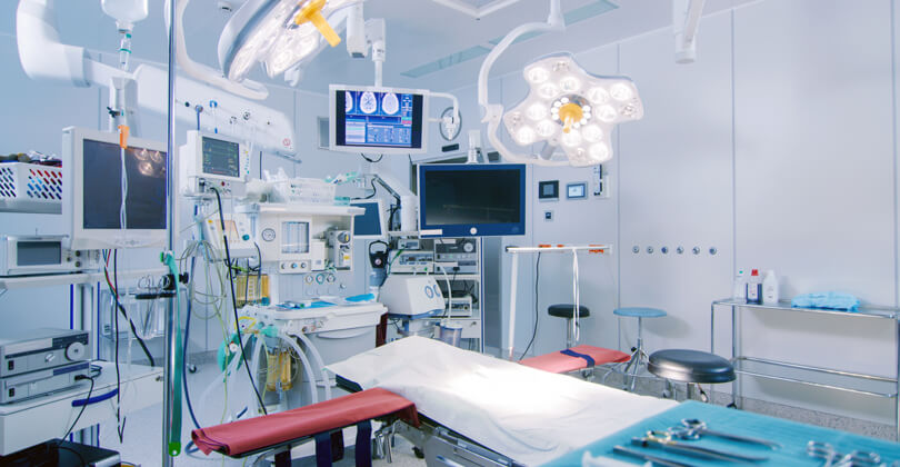 Picture of a modern operating room, representing the medical facilities available in San Jose, Costa Rica.  The picture shows an operating table and extensive medical equipment to the side and above the table.