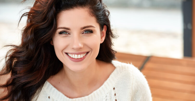 Close-up picture of a beautiful female patient, happy with the nose surgery she had at Frontline Plastic Surgery in San Jose, Costa Rica.  The picture shows a woman with dark brown hair and wearing a white blouse, smiling while looking directly at the camera.